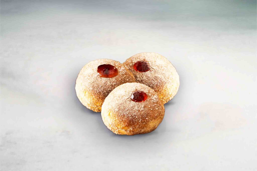 Three freshly baked and fried fun-sized donuts filled with jam, offering a crispy exterior and a sweet jam-filled interior.