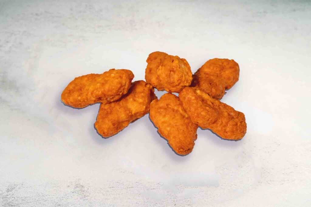 A plate of 6 golden, crispy chicken nuggets with a side of tomato sauce dip.