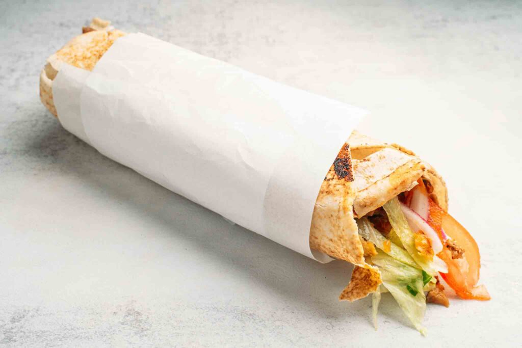 Delicious kebab wrapped in warm pita bread with tender lamb, chicken, or falafel, topped with fresh vegetables, and drizzled with creamy garlic sauce, ready to enjoy