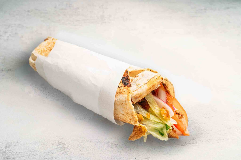 Small-sized kebab with tender meat or falafel, fresh vegetables, and garlic sauce, wrapped in warm pita for a tasty snack.